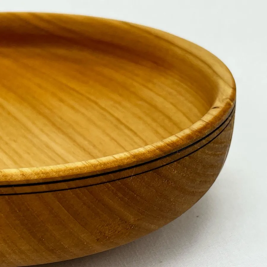 Close detail of a golden wooden bowl, its curved rim following the natural grain